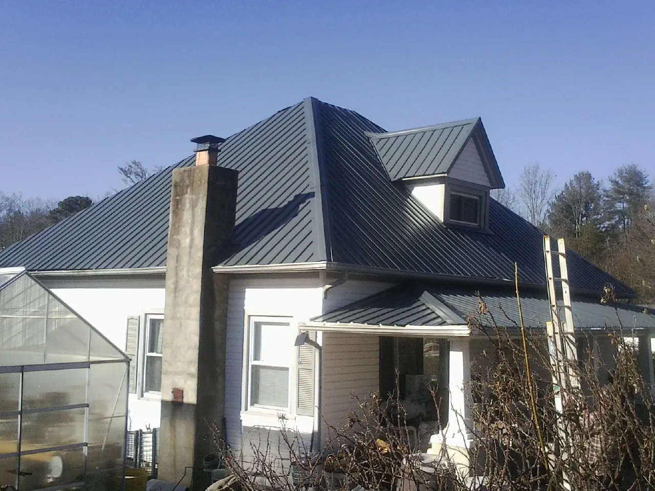 Dark blue standing seam metal roof on a white farmhouse with dormer — Slate & Tile Roof Repair by Roofing Brothers in Lyles