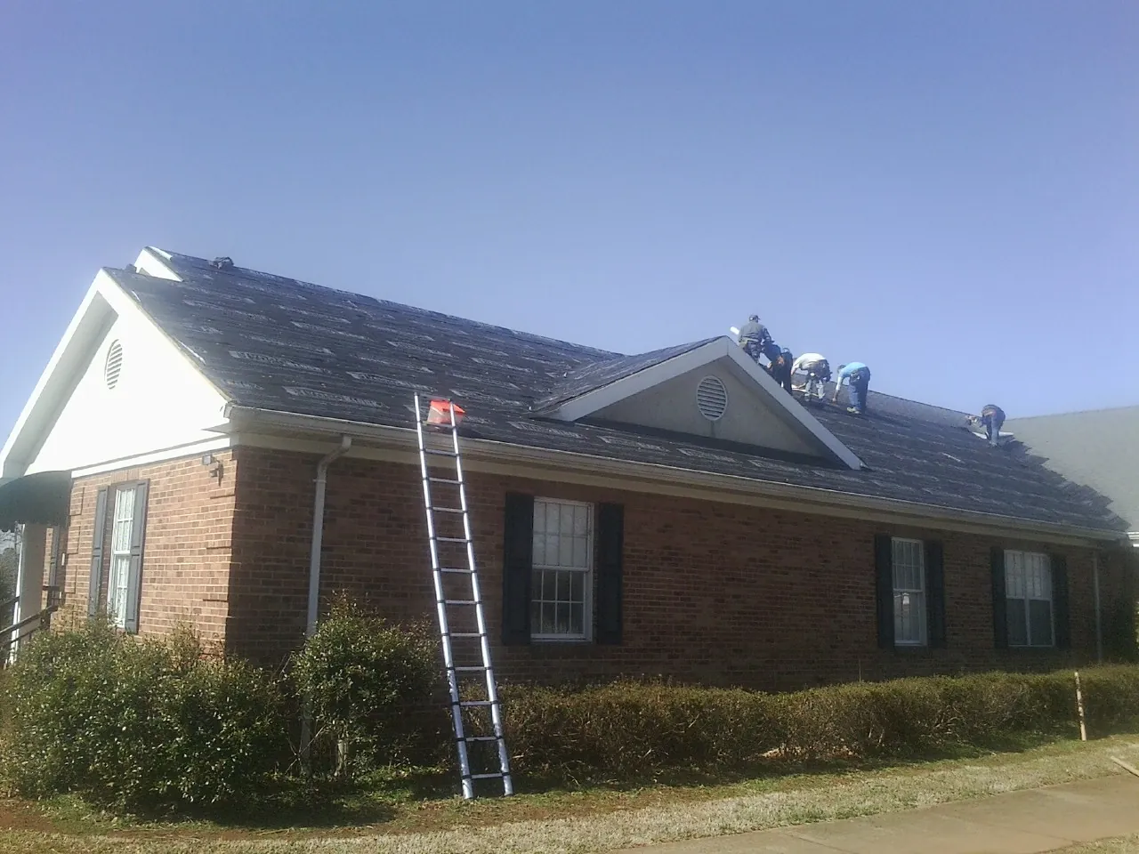 Crew tearing shingles off a brick ranch roof with a ladder set — Emergency Roof Repair work by our crew in Lyles