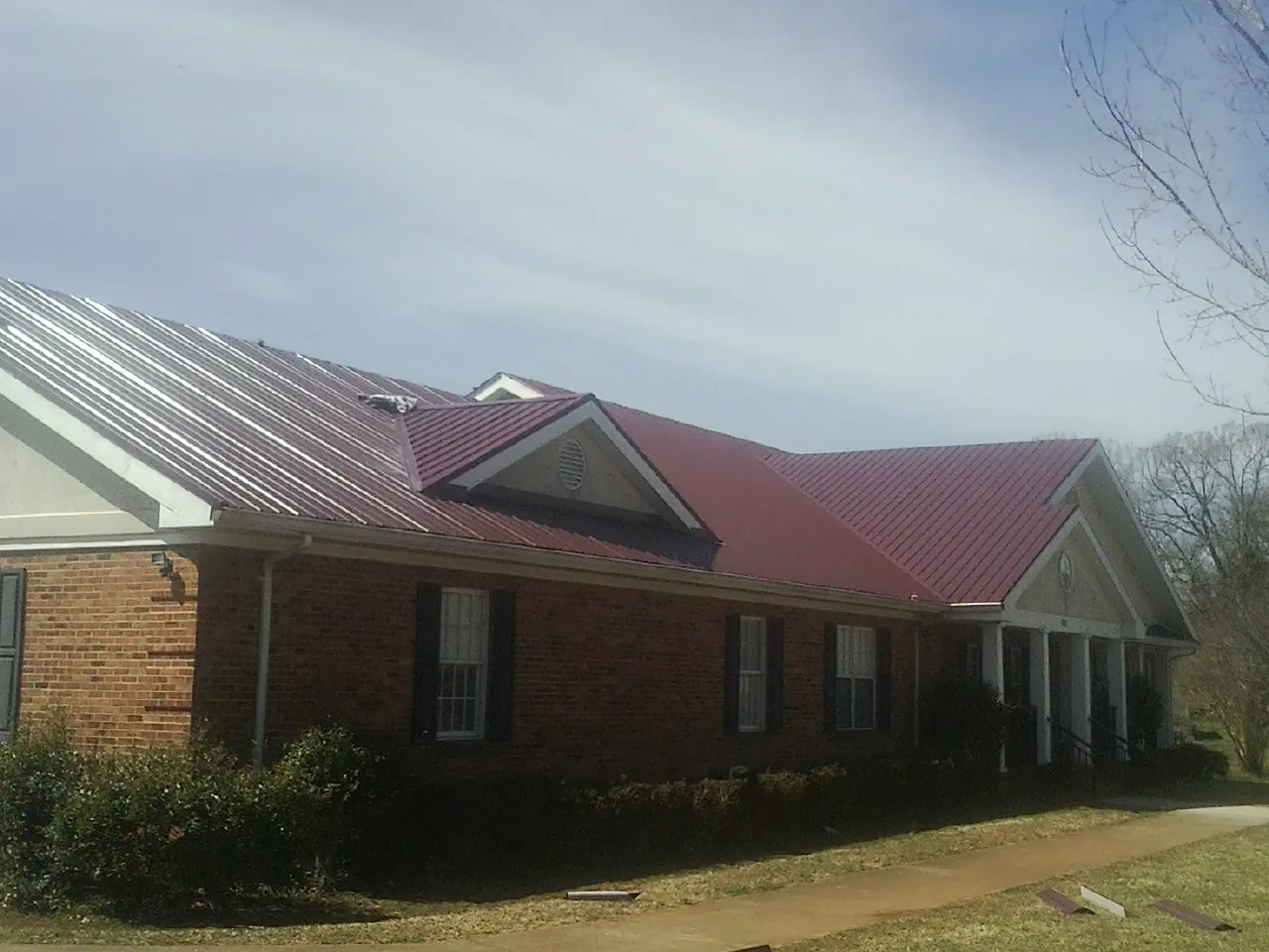 Red metal roof with gabled entries on a long brick building, from a Hail Damage Roof Repair job in Lyles