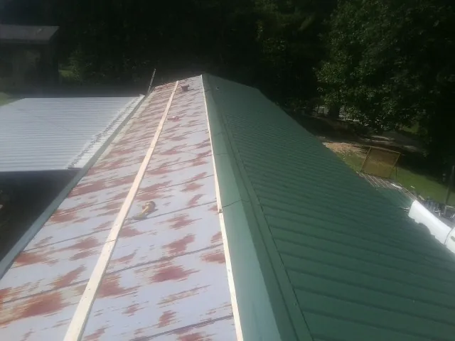 Old rusted panels beside newly installed green metal roofing — Wind Damage Roof Repair by Roofing Brothers in Lyles