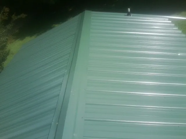New green metal panels meeting at the ridge of a roof — Flat Roof Repair work by our crew in Lyles