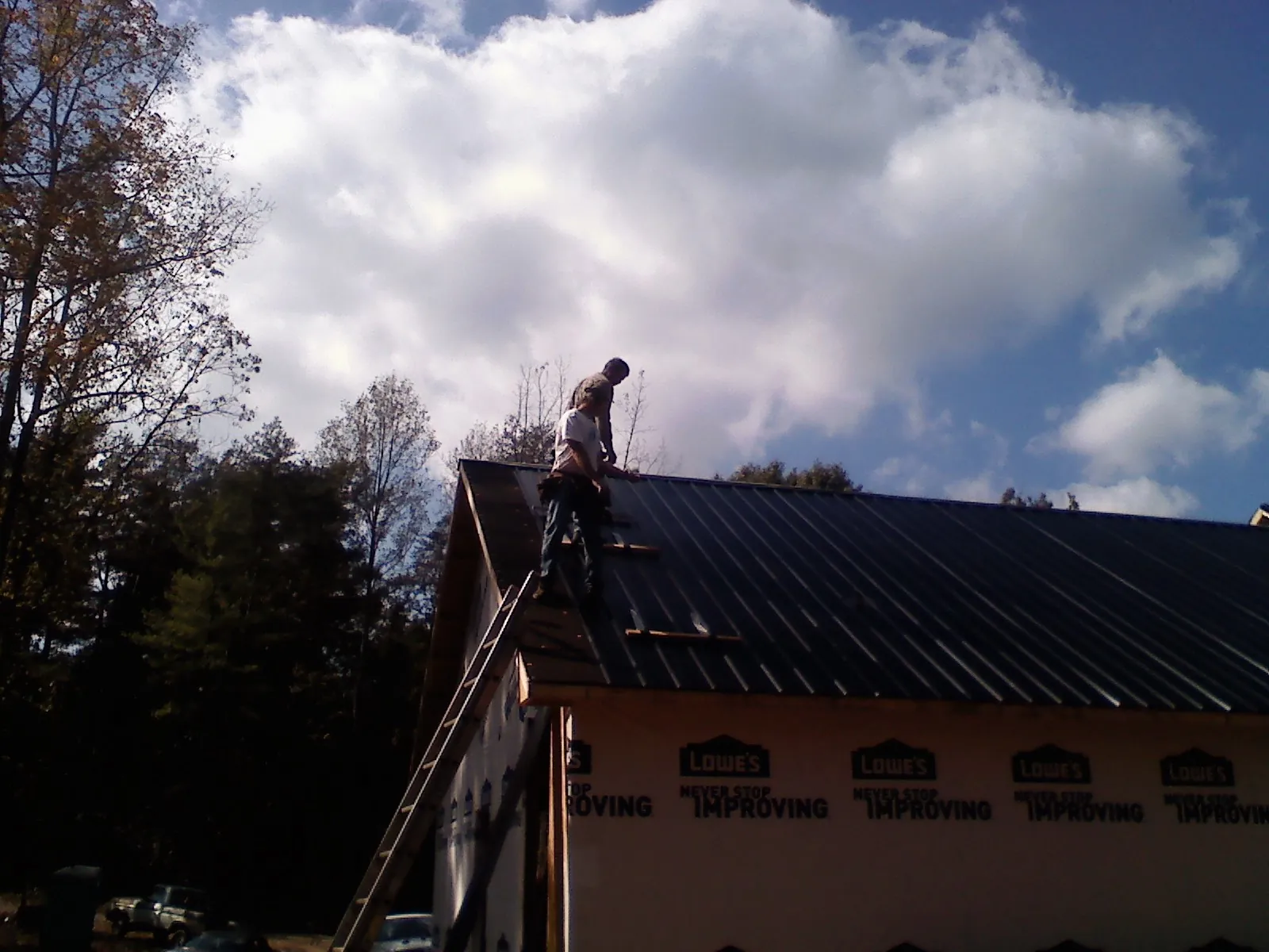 Roofer fastening dark metal panels high against a cloudy sky in Lyles