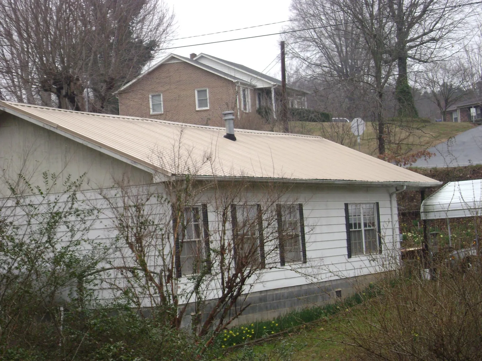 Tan metal roof on a white sided house set into a hillside — Commercial Roofing by Roofing Brothers in Lyles