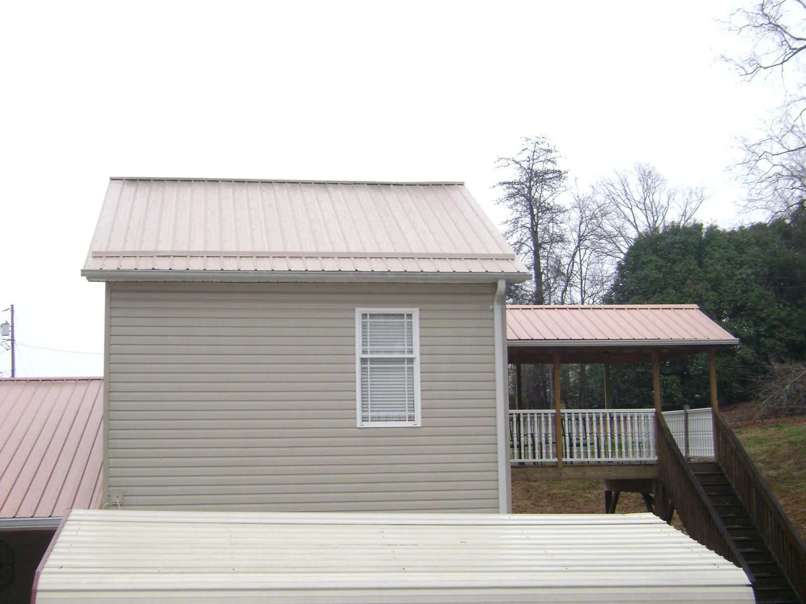 Tan metal roofs on a two story addition and attached porch, from a Roof Replacement job in Lyles